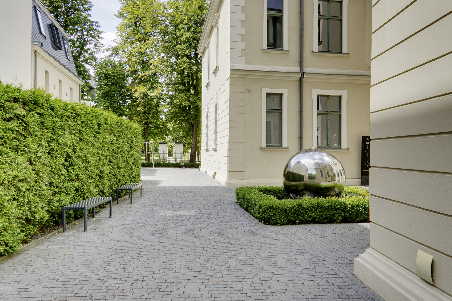 Dziedziniec kompleksu biurowego przy Libelta 27 z metalową rzeźbą kuli pośród zieleni
