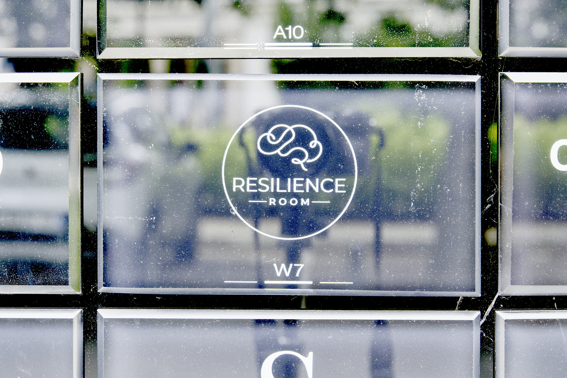 Grawerowane oznaczenie Resilience Room i numer gabinetu W7 na szklanej tabliczce przy wejściu